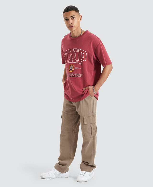Man wearing a maroon red box fit t-shirt with ribbed crew neckline printed with a large Nena and Pasadena x Carlton Draught logo, paired with brown cargo pants.